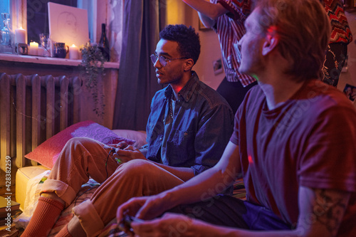 Two young men sitting on the floor and playing video games together during domestic party