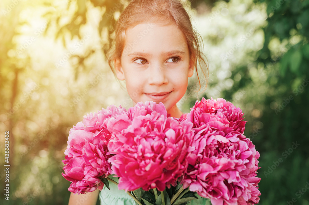 portrait of a happy cute little caucasian seven year old kid girl, holds in hands a bouquet of pink peony flowers in full bloom on the green background of nature. flare