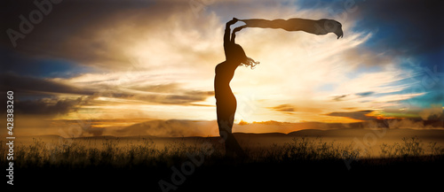 Obraz na plátně Silhouette of a girl waving her shawl in the wind during a warm summer sunset in the mountains