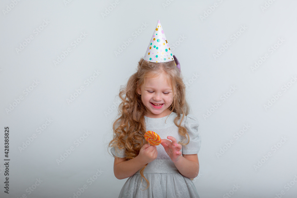 little girl in a birthday hat with a lollipop on a white background studio