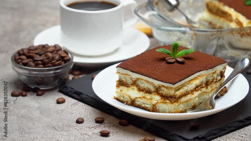 Traditional Italian Tiramisu dessert in glass baking dish and portion on grey concrete background Traditional Italian Tiramisu dessert in glass baking dish and portion on grey concrete background