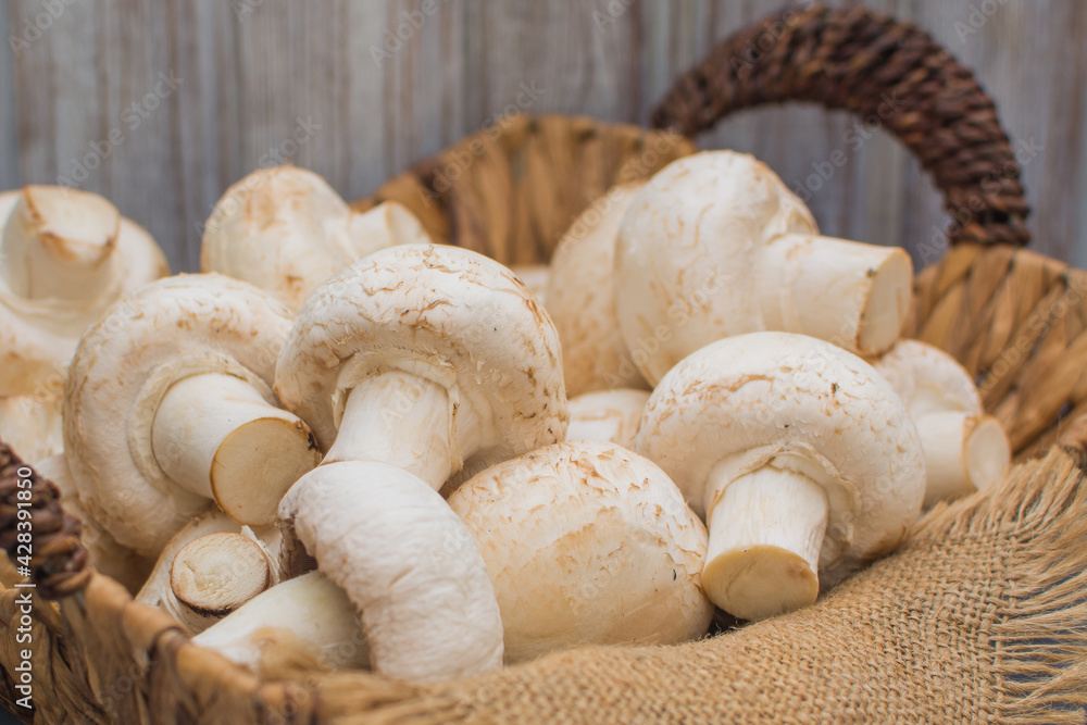 Fresh champignons in a wicker basket on a dark wooden background.