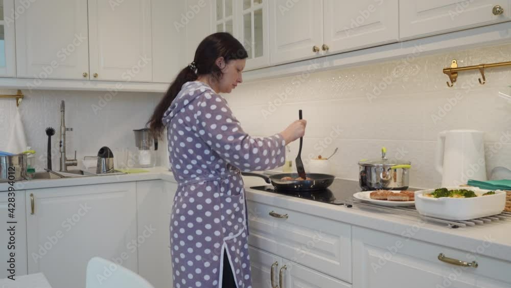Woman cooking meals for dinner in modern white clean kitchen frying cutlets on electric stove. High quality 4k footage Woman cooking meals for dinner in modern white clean kitchen frying cutlets on electric stove. High quality 4k footage
