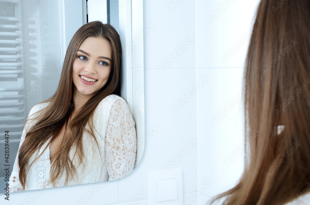 Young woman in bathroom. Polish model smiling in the mirror reflection.