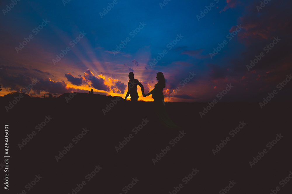 Fototapeta premium pregnant woman and her husband walking in the sunset