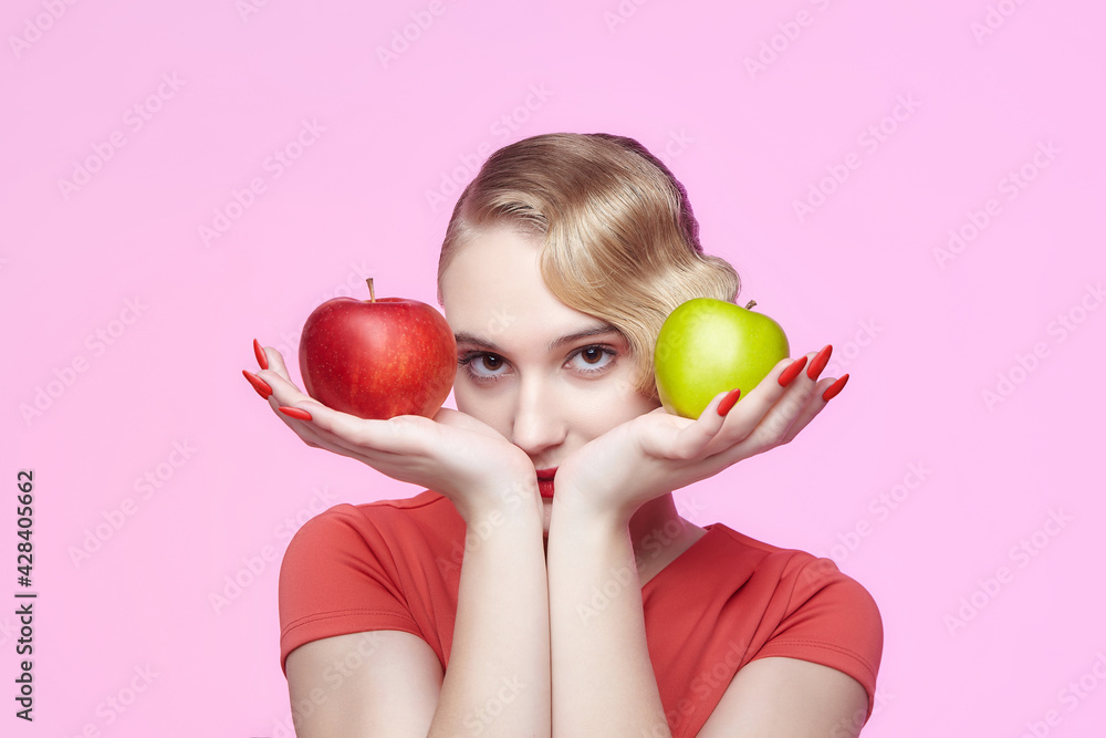 attractive young blonde with a retro hairstyle holds a red and green apple in front of her face attractive young blonde with a retro hairstyle holds a red and green apple in front of her face
