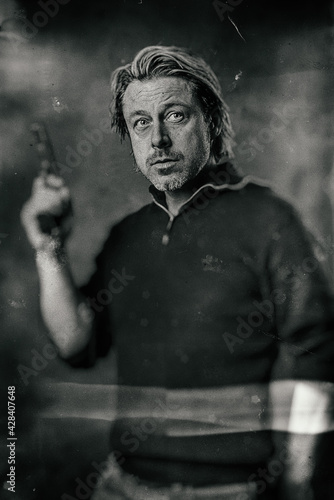 Vintage wet plate portrait of blond man with stubble beard and handgun in sweater.