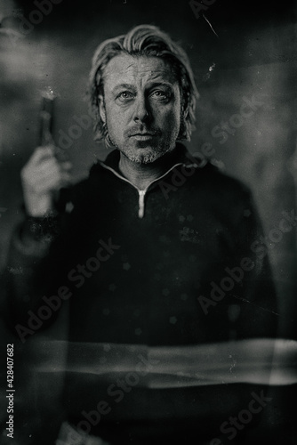 Vintage wet plate portrait of blond man with stubble beard and handgun in sweater.