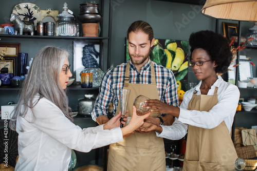 Mature woman choosing decor at modern store and consulting with two multiracial workers. Professional sellers in uniform providing service for customer.