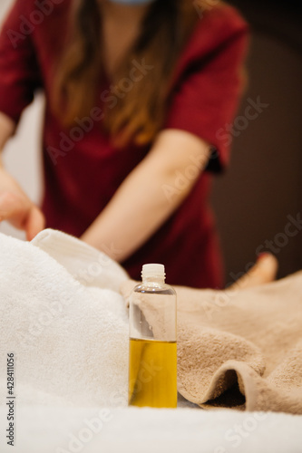 Yellow massage oil in a bottle. On background: masseuse strech and massages the client's body. Spa relaxation treatments
