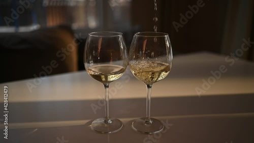 Wallpaper Mural Pours white dry wine into a one of two glasses standing on white table. Defocused blurred background. Close up slow motion video of wine mixing process inside goblet with sun light.  Torontodigital.ca