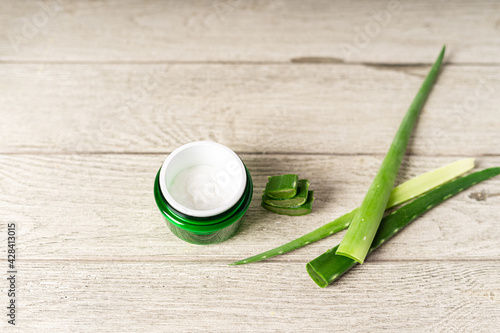 Fresh aloe vera plant, stem slices and gel in glass jar on wooden background, skin therapy, natural organic cosmetic concept.