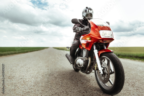 Man rides a red motorcycle on a country road