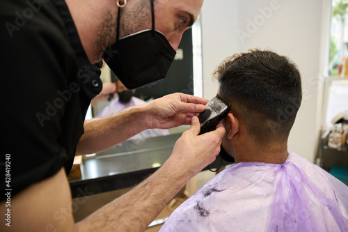 Barber cutting man hair with clipper wearing mask