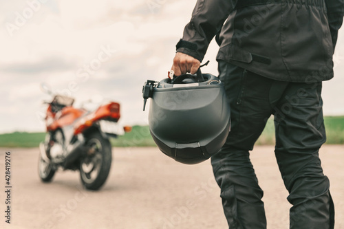 A man walks to his motorcycle, holding a helmet in his left hand. Motorcycle helmet close up