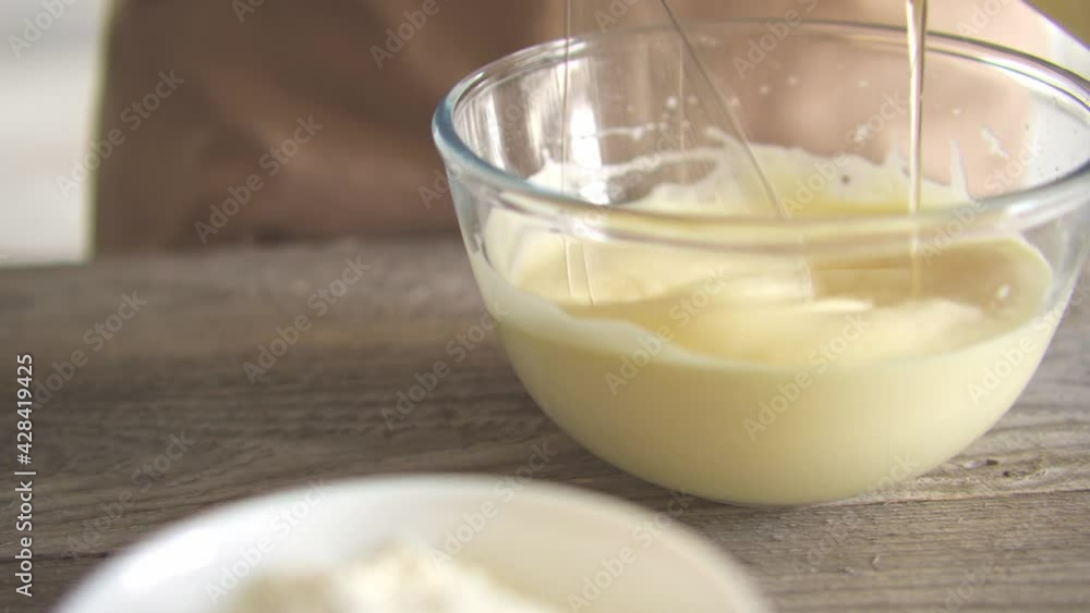 Pouring sunflower oil into beaten egg yolks for baking in the kitchen. The cook is pouring sunflower oil into a glass bowl. Pouring sunflower oil into beaten egg yolks for baking in the kitchen. The cook is pouring sunflower oil into a glass bowl.