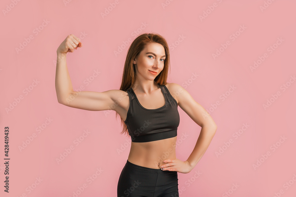 Fitness girl smiling in black sportswear on a pink background. Slim woman with a beautiful athletic body and tanned skin Fitness girl smiling in black sportswear on a pink background. Slim woman with a beautiful athletic body and tanned skin