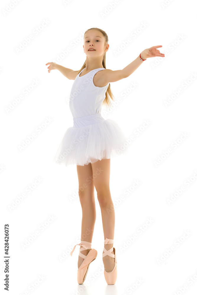 Cute little girl in a tutu and pointe shoes dancing in the studio on a white background.