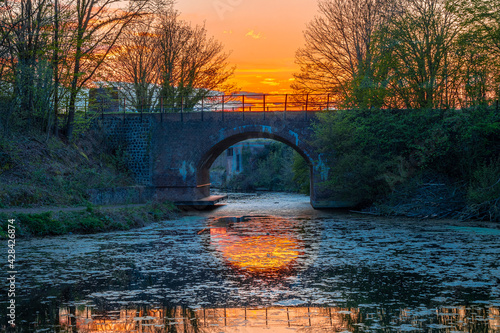 Colorful sunset and reflections in the water in the Frontenpark (English: Fronten Park) in Maastricht. This park is recently re-opened after restorations of the ancient walls and the old train bridge photo