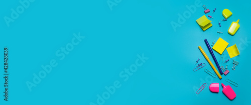 Stationery items on the blue background with free space for text. Creative, colorful background with scool or office supplies. Flatlay with copy space, top view. Markers, paper clips, sticky notes. photo