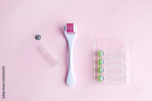 derma roller, meso scooter, gold micro needles and hyaluronic acid ampoules on a pink background. Anti-aging care for the skin of the face, neck and neckline area, anti-cellulite effect. photo