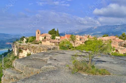 Village with romanesque church of Santa Maria de Siurana on top of rock, view into valley, mountains on the background. Blue sky with white clouds.  Siurana, Catalonia, Spain.