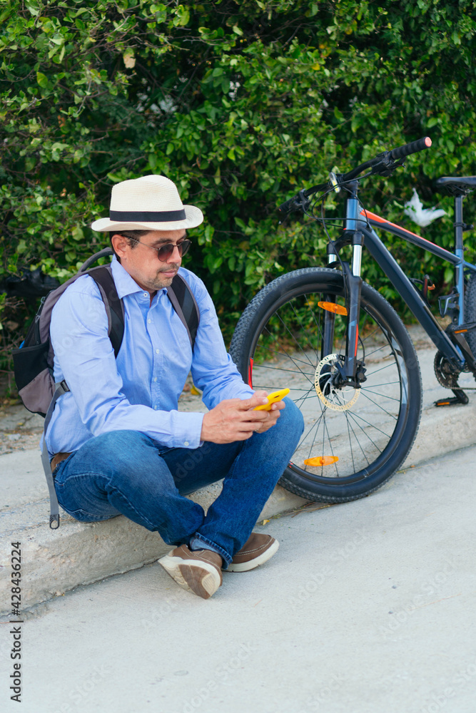 Obraz premium 40-year-old man checking his cell phone while sitting on the street with his bicycle