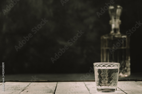 Vodka in decanter and shot glass on wooden plank table.