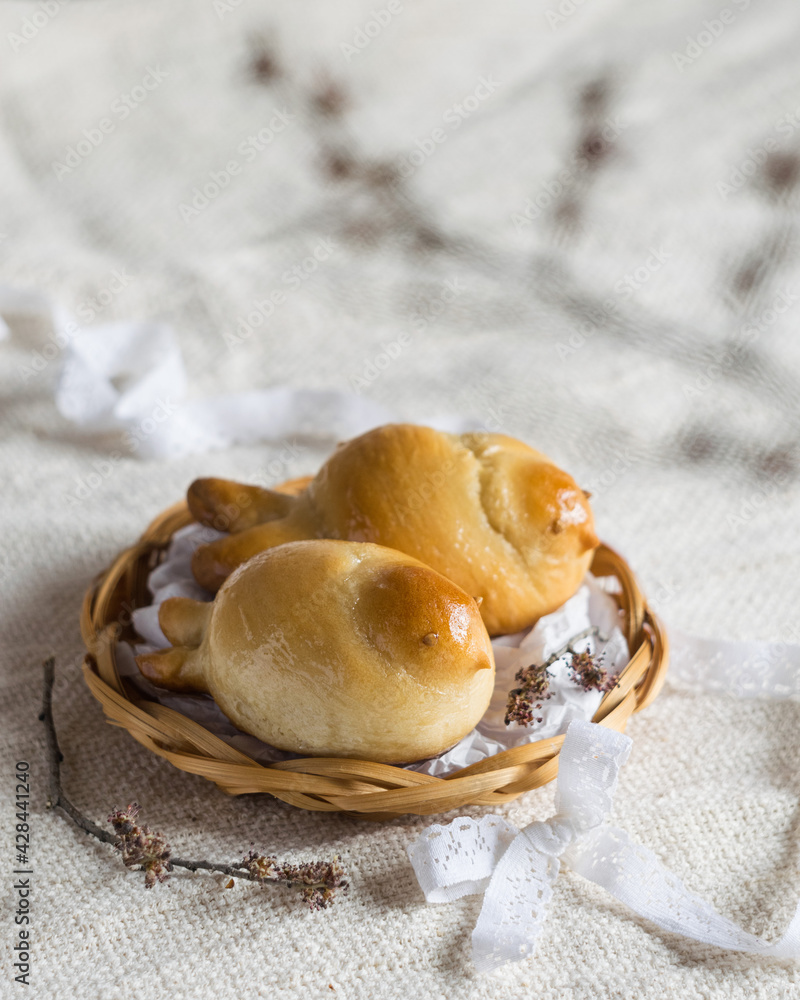 Two easter bird-shaped lean buns coated with sweet syrup on a plate on light textile, selective focus, rustic style.