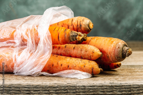 Carrots in transparent bag on table. Buying vegetables in store. Autumn harvest in garden. Ingredient for vegetarian diet, salad preparation. Plastic packaging is harmful to environment