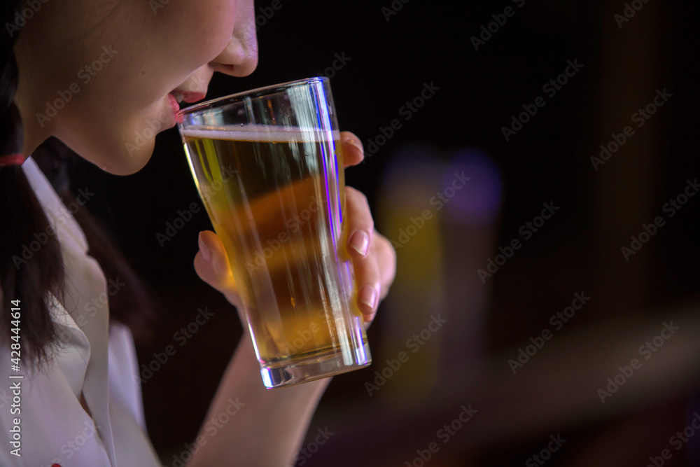 Beautiful Asian woman holding a glass of beer close up on background inside bar. Beautiful Asian woman holding a glass of beer close up on background inside bar.