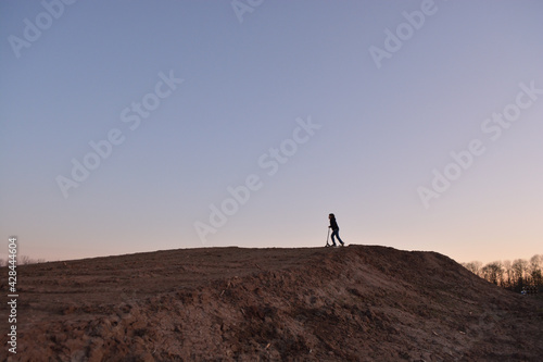 Silhouette of a playing boy with a roller playing with a scooter on a earthy hill at sunset © Julia