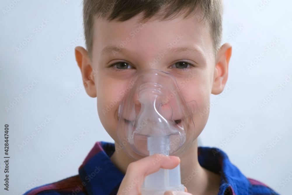 Portrait of happy smiling child boy is breathing in mask using nebulizer for inhalation procedure at home. Fibrosis, covid-19, asthma, copd. Treatment, cure and procedure. Using inhaler for therapy.