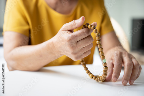 Asian senior woman praying and meditating with religious rosary, concept of social distancing religious service at home, praying at home