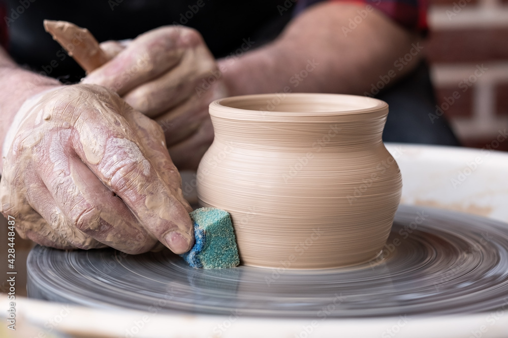 Male hands cleaning with sponge pottery on a potter wheel.