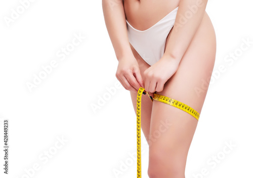 Diet - young woman is measuring her thigh with measuring tape on white background