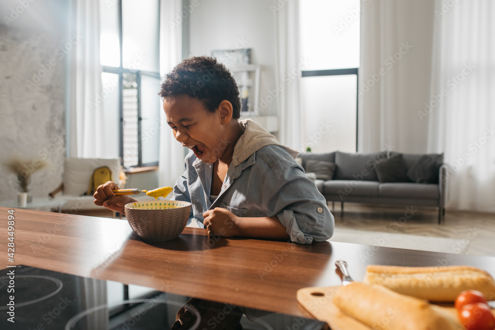 Boy open his mouth widely while bringing a spoonful of soup to his face Boy open his mouth widely while bringing a spoonful of soup to his face