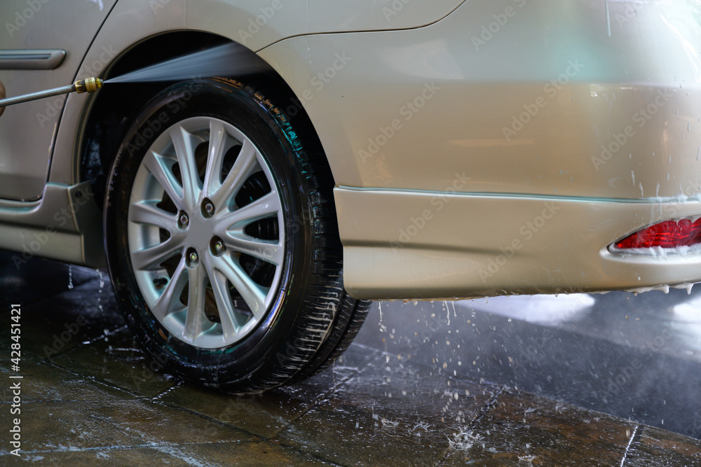 Young asian man Washing the car and spraying the wheels under high pressure water at a car wash service station.