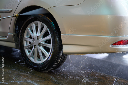 Young asian man Washing the car and spraying the wheels under high pressure water at a car wash service station.