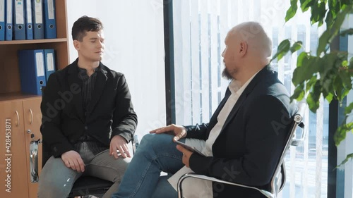 Portrait of two businessman sitting and chatting with office background. Casual looking men in suits discussing oportunities and upcoming projects. Concept of interview, deal. photo