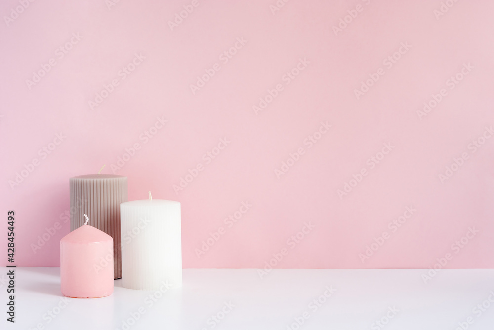 Three pastel colored candles on a table across pink backround with copy space for text or image Three pastel colored candles on a table across pink backround with copy space for text or image