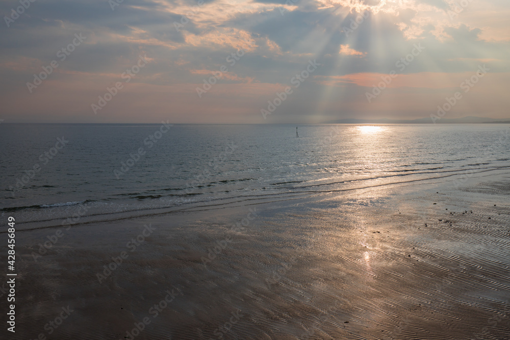 Dramatic sky with sun rays above Colwyn bay, North Wales. Dawn sunrise on the coast with a calm sea