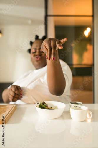 Woman putting salt into fresh vegetarian salad while sitting at the kitchen