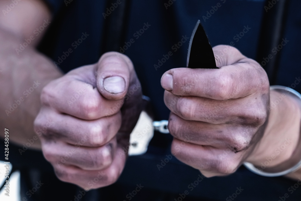 Fototapeta premium Close up handcuffed man with a knife imprisoned for crime, punished for serious villainy. Arrest, gangster, pain concept. Selective focus.