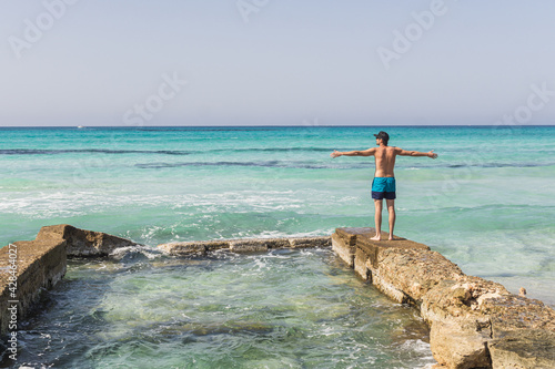 Man standing in sweamwear in front of the sea raised his hands up enjoying the holidays.