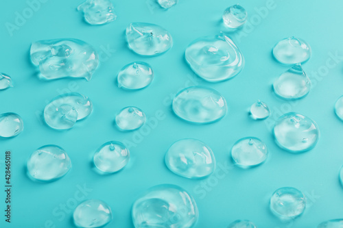 Drops of Gel with hyaluronic acid in the form of a smear of glossy texture on a cyan background.