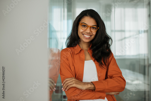 Portrait of  smiling African American business woman wearing stylish eyeglasses looking at camera standing in modern office. Successful business and career concept 