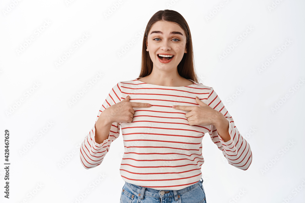 Surprised happy girl pointing at herself, pleased to be chosen, winning something, hear great news about her, standing over white background Surprised happy girl pointing at herself, pleased to be chosen, winning something, hear great news about her, standing over white background