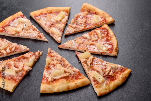 Tasty fresh oven pizza with tomatoes, cheese and pineapple on a dark concrete background