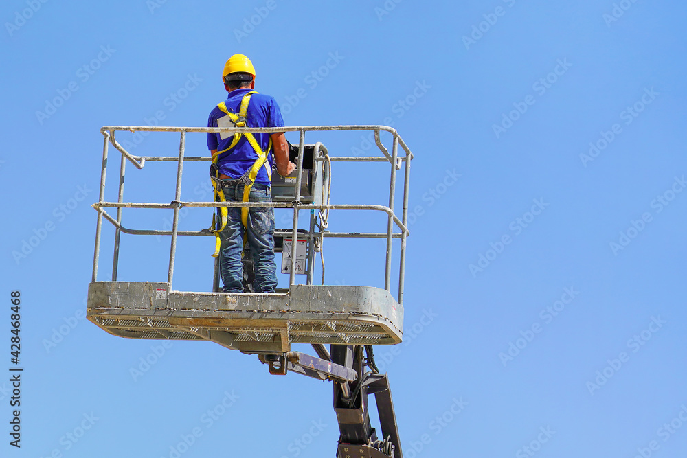Electrician in the cart. Worker in a safety helmet and safety equipment in a lifting trolley Electrician in the cart. Worker in a safety helmet and safety equipment in a lifting trolley
